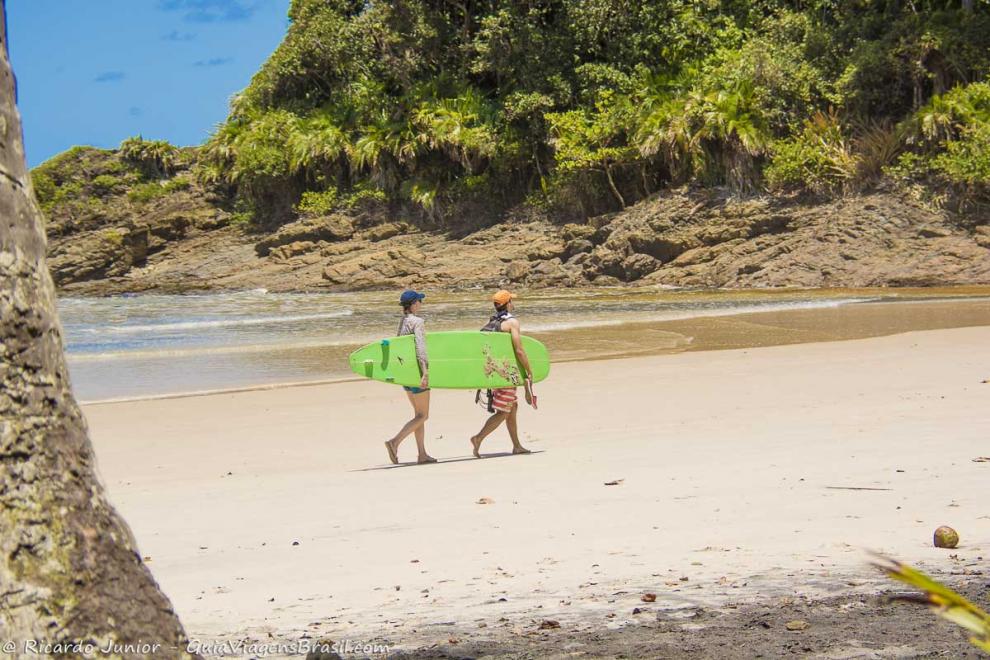 Imagem de uma casal carregando prancha próximo ao canto da Praia da Engenhoca.
